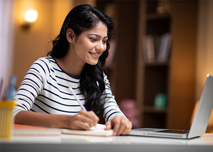 A lady sitting with laptop and writing notes