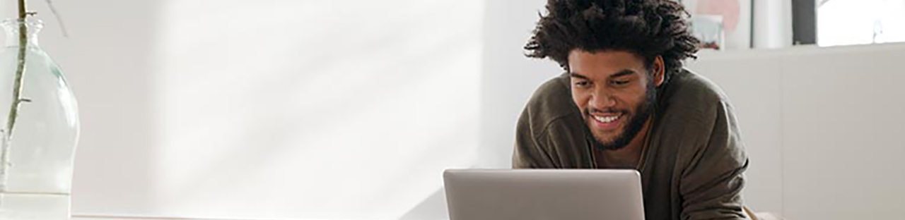 Homme assis dans un bureau, regardant l’ordinateur portable et souriant