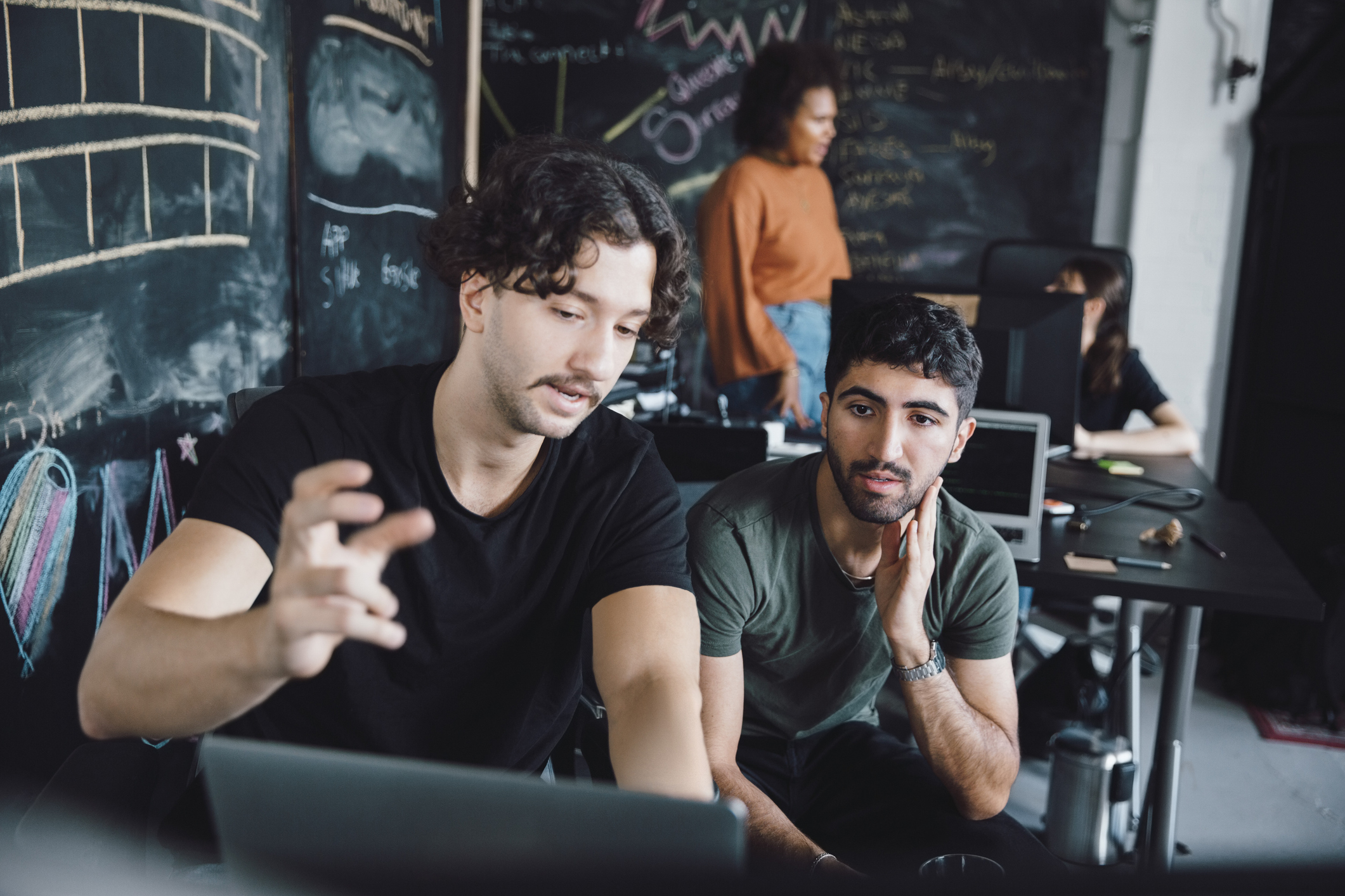 In a classroom, one college student instructs another college student as they look at a computer screen