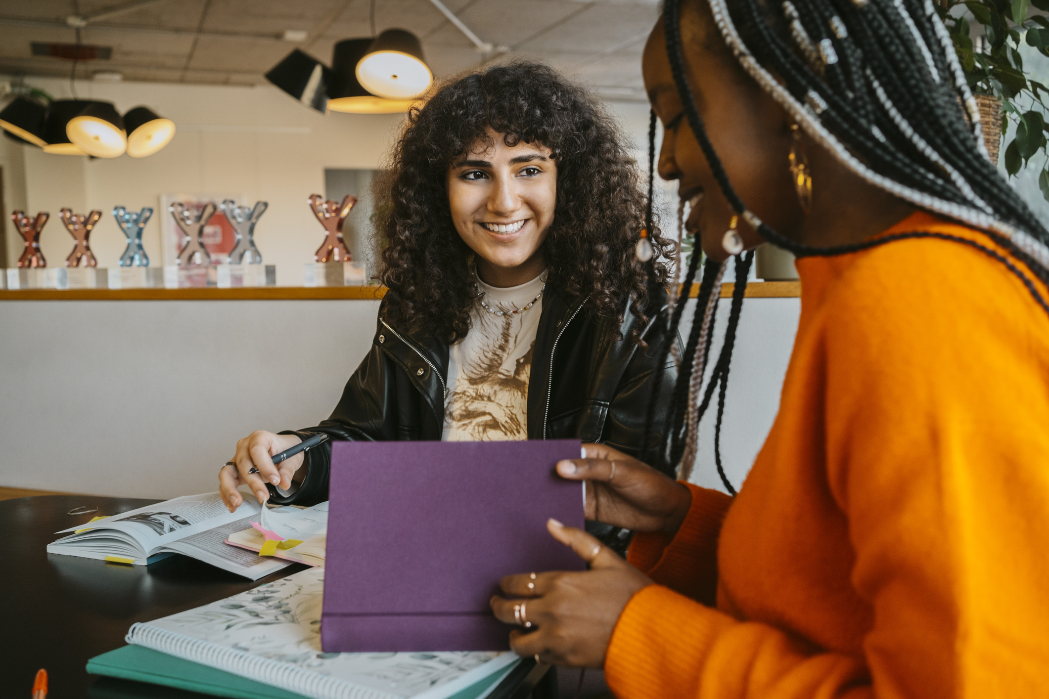 Two college women smile in conversation as they study over their textbooks